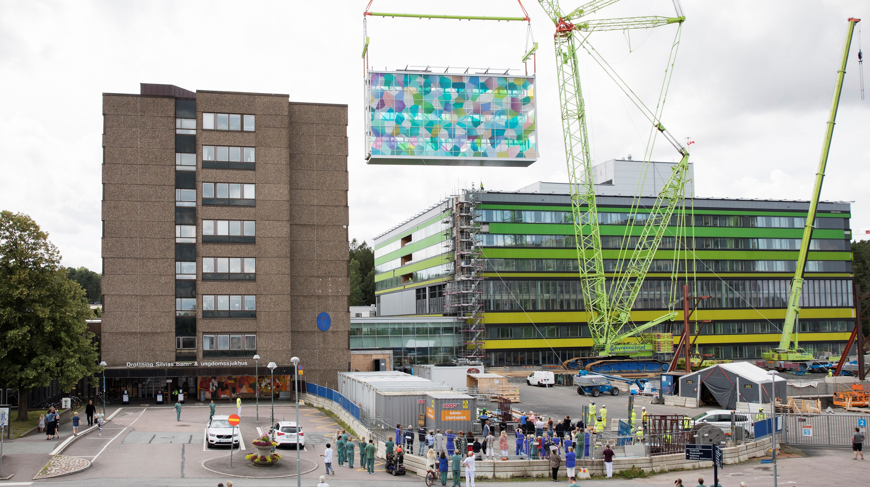 Förbindelsegången mellan det nya och gamla barnsjukhuset lyfts på plats av en kran. Många människor tittar på.