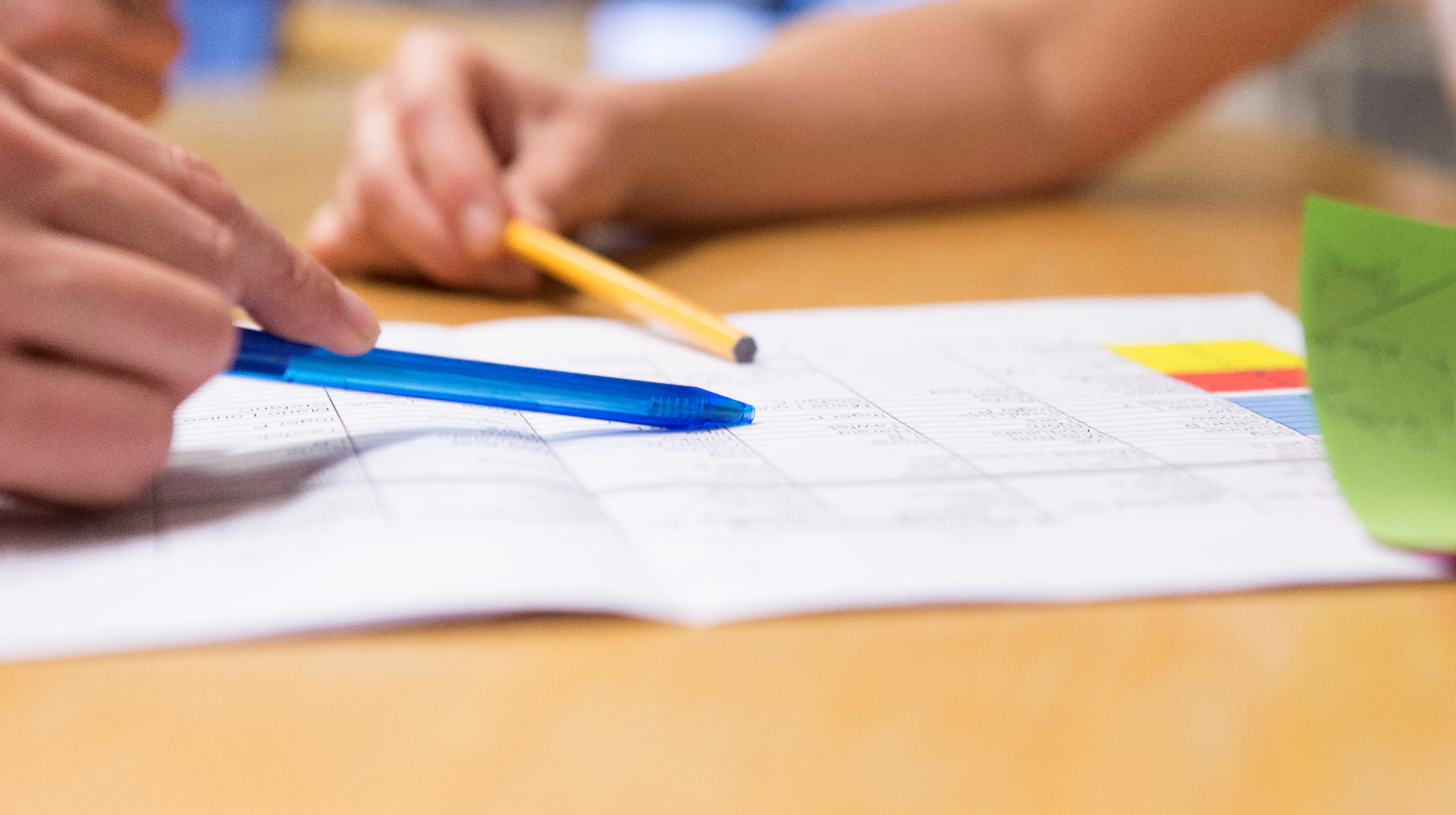 Detaljbild av två händer med pennor som pekar på ett papper.