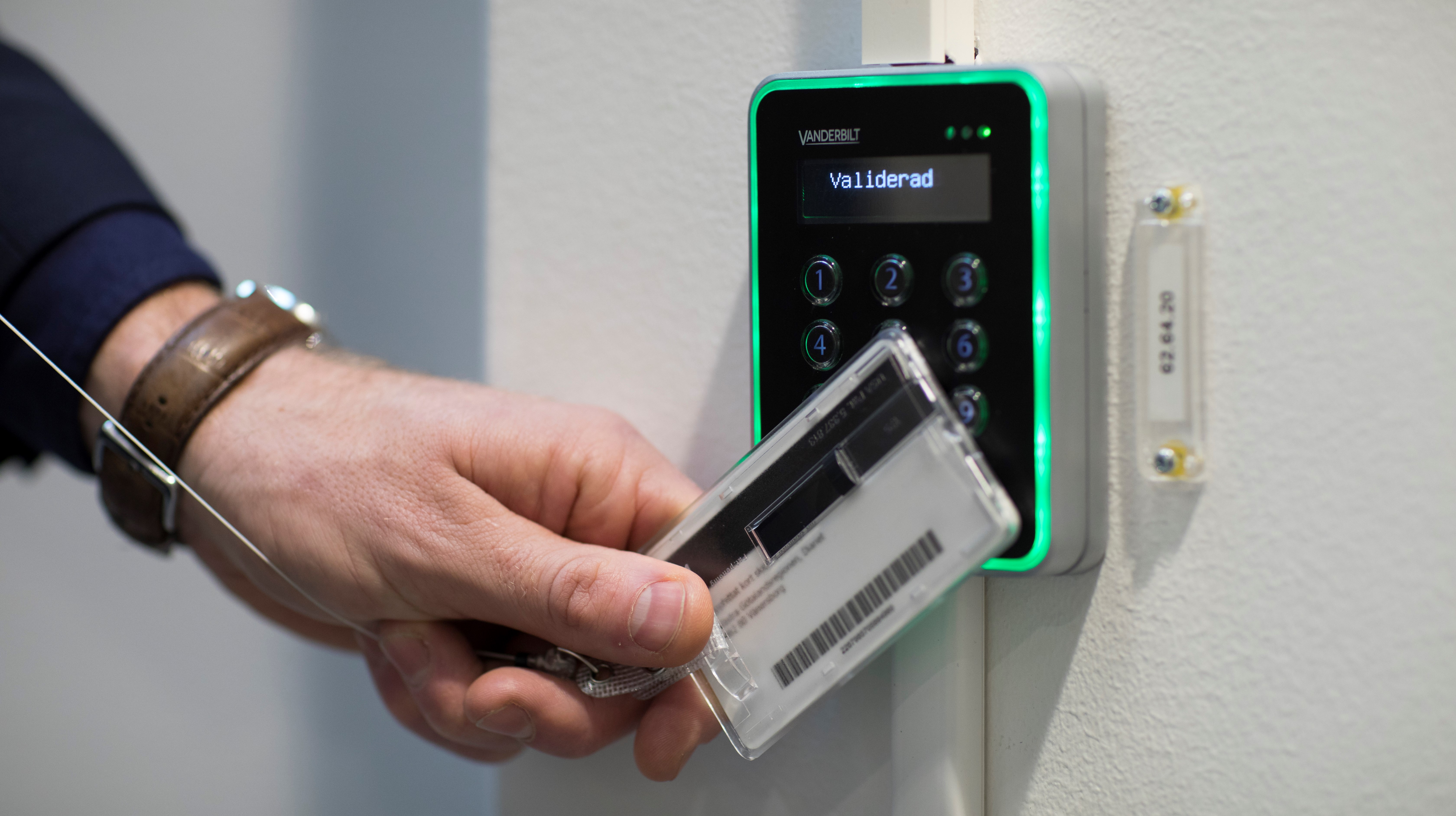 Detaljbild på ett kodlås och en hand som håller upp sitt kort mot låset.